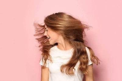 Frau schüttelt ihr langes Haar vor rosanem Hintergrund