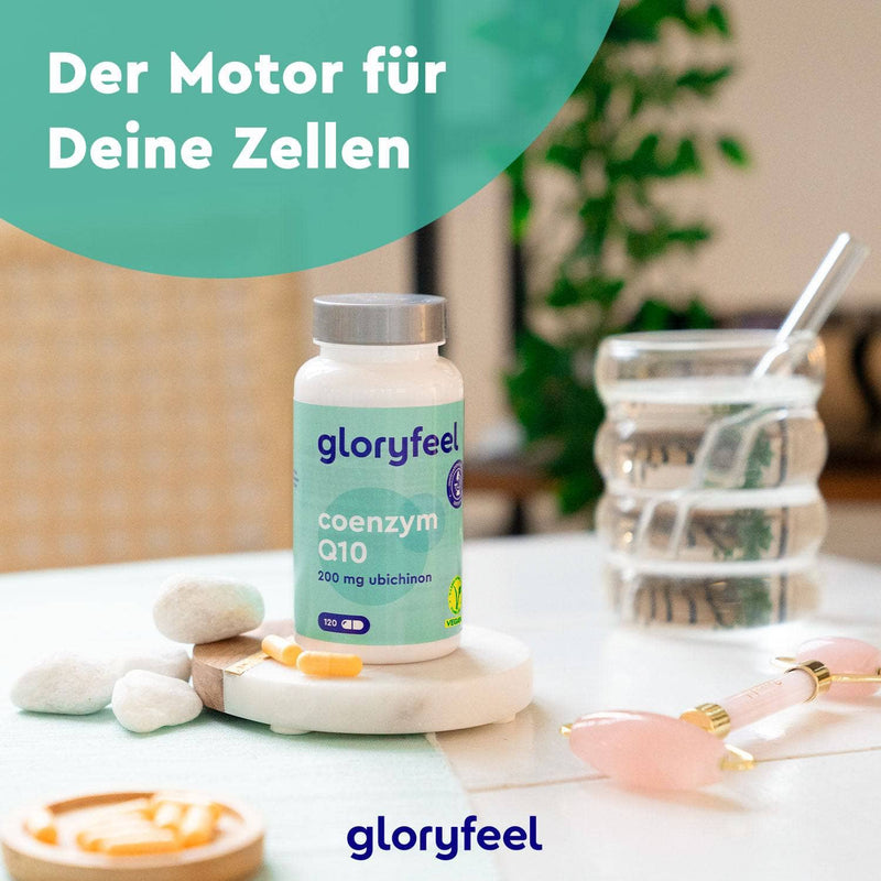 Eine Flasche Coenzym Q10 Kapseln der gloryfeel GmbH steht auf einem Tisch mit Spa-Artikeln und einem Glas Wasser. Auf dem Etikett steht „Der Motor für Deine Zellen“.