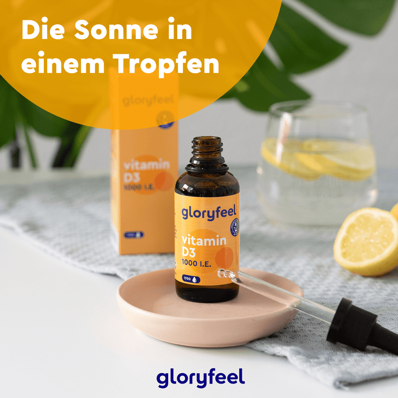 Eine Flasche Vitamin D3 Tropfen 1000 I.E. der gloryfeel GmbH steht mit einer Pipette auf einem kleinen Teller, umgeben von einem Glas Zitronenwasser und Zitronenscheiben auf dem Tisch. Der deutsche Text lautet: „Die Sonne in einem Tropfen.“.