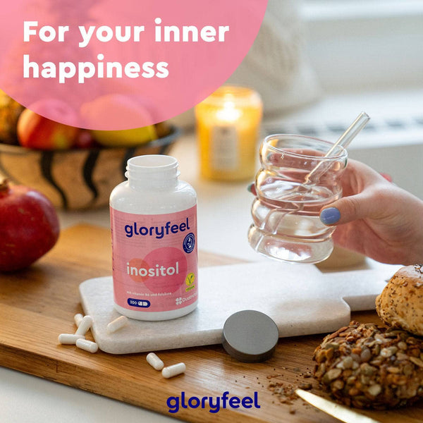 Inositol-Kapseln der gloryfeel GmbH stehen zusammen mit Kapseln, einem Glas Wasser und einer Kerze auf einer Küchentheke. Text: „Für dein inneres Glück.“.
