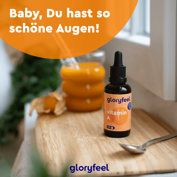 Eine Flasche mit der Aufschrift „Vitamin A Tropfen“ der gloryfeel GmbH steht auf einer Holzfläche neben einem Glas Orangensaft und einer Pflanze. Der Text „Baby, Du hast so schöne Augen!“ in einem orangefarbenen Kreis unterstreicht die Vorteile von Beta-Carotin für schöne Augen.