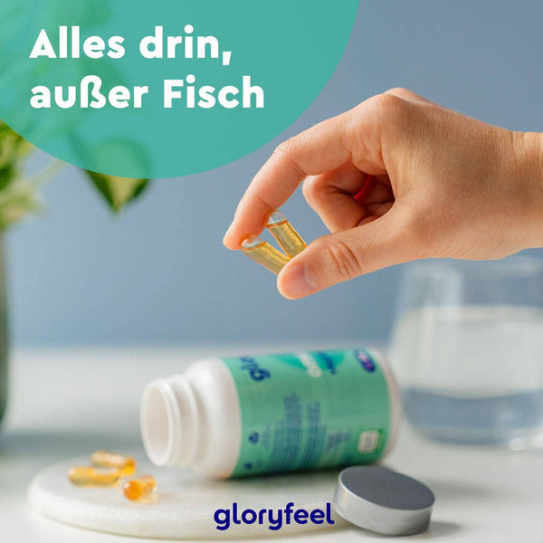 Eine Hand hält eine Kapsel über einer Nahrungsergänzungsmittelflasche mit der Aufschrift „Alles drin, außer Fisch“ der gloryfeel GmbH. Diese veganen Omega-3-Kapseln sind reich an EPA und DHA.