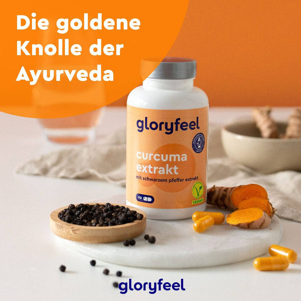 Eine Flasche Curcuma Extrakt Kapseln der gloryfeel GmbH steht mit Kurkumascheiben und schwarzen Pfefferkörnern auf einem Tisch, im Hintergrund sind eine weitere Kurkumawurzel und ein Glas zu sehen. Der Text lautet: „Die goldene Knolle des Ayurveda.“.
