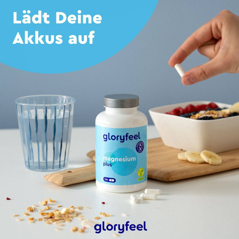 Eine Hand hält eine Kapsel über einem Tisch mit einer Magnesium Plus Kapseln-Flasche der Gloryfeel GmbH sowie Obst, Wasser und Haferflocken. Der Text lautet: „Lädt Deine Akkus auf.